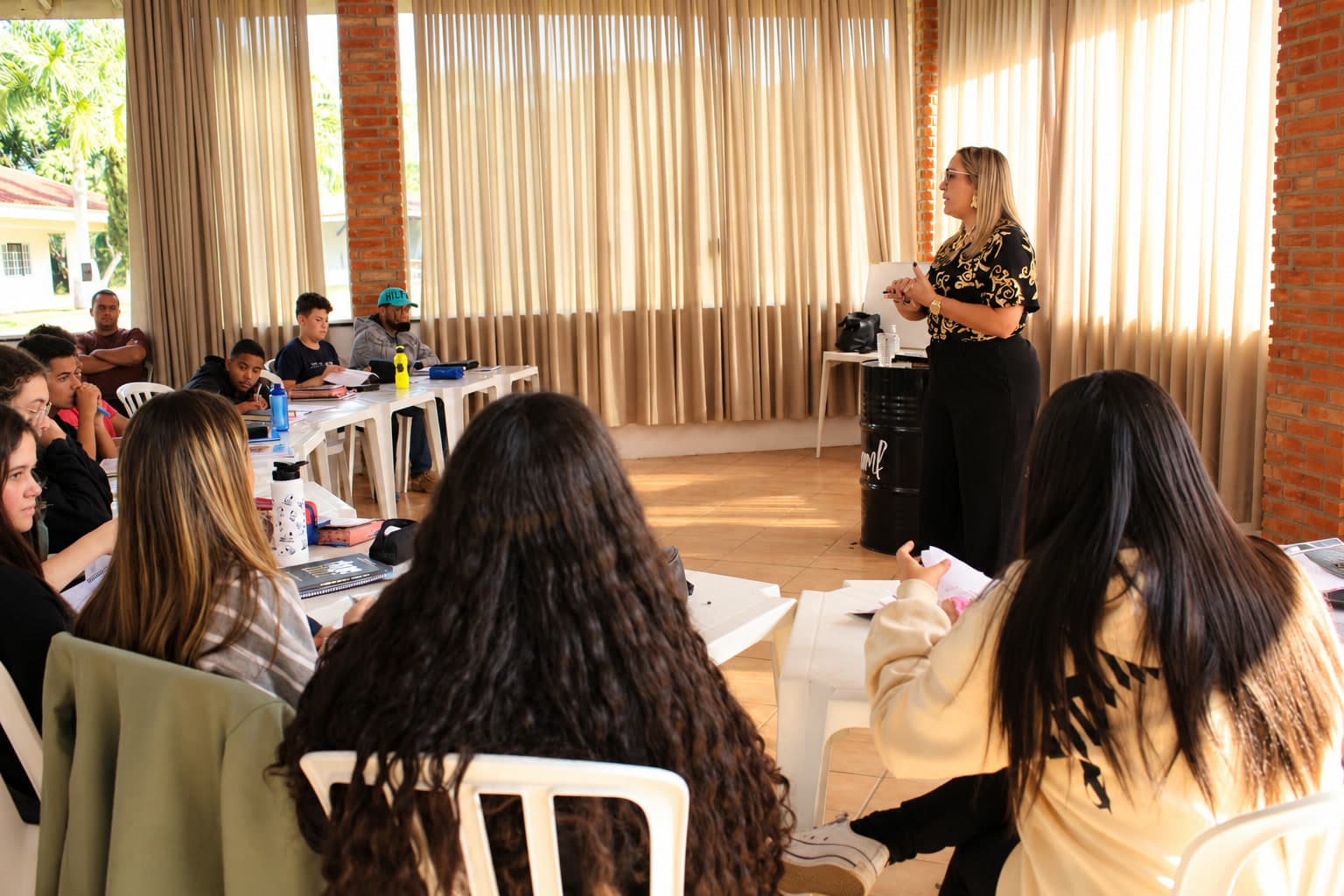 Professora dando aula para alunos da ESCAMF Urbana sentados em volta das mesas